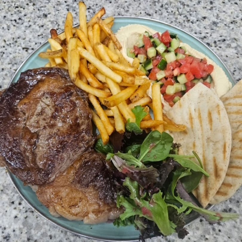 Grilled steak, french fries, hummus with diced vegetables, salad, and pita bread on a blue plate.