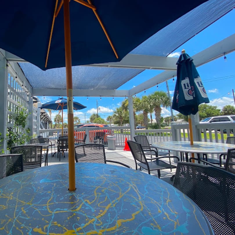 Outdoor patio dining area at Gili's Kitchen with blue umbrellas, tables, and chairs under a sunny sky.