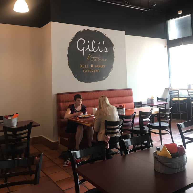 Two women dining at a booth in Gili's Kitchen, with tables and chairs filling the restaurant.