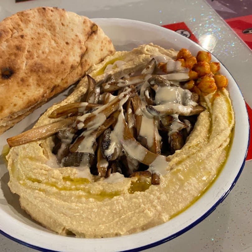 A bowl of Gili's Kitchen hummus topped with mushrooms, chickpeas, and a side of pita bread.